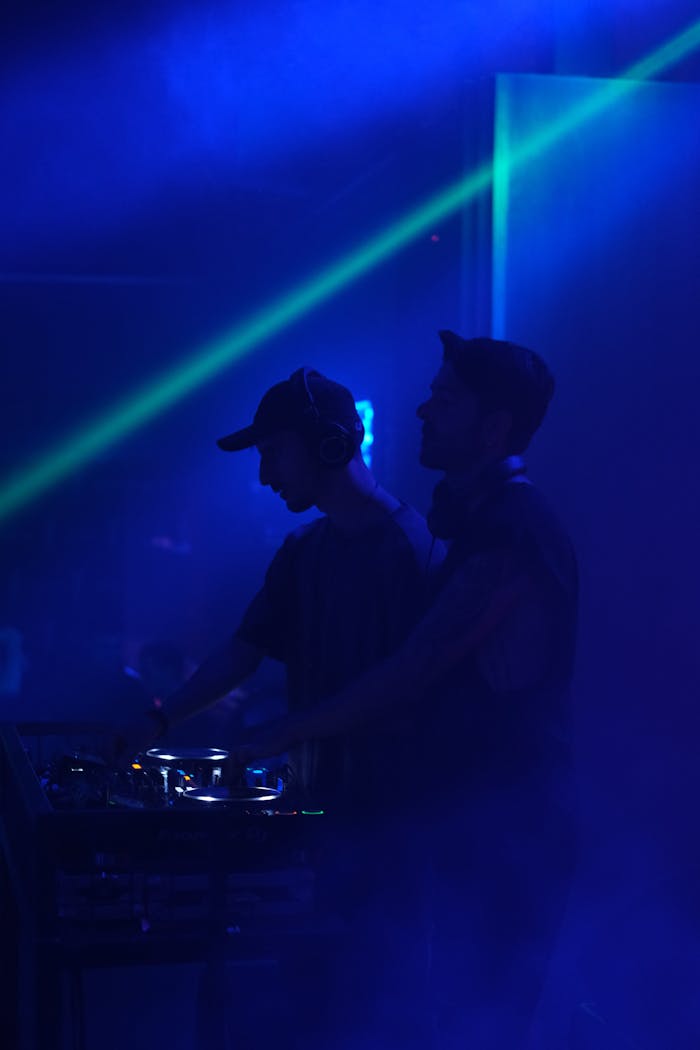 Rhythm of the afterlife Two DJs performing live on stage in a neon-lit environment, spinning tracks with audio equipment.